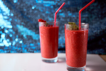 Strawberry and banana smoothies with long glasses on white plate. Blue background