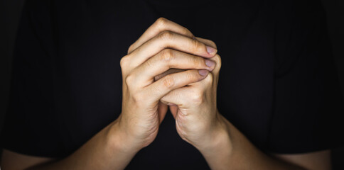 Praying hands of young man in the shadow.
