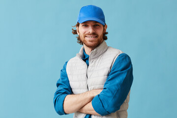 Portrait of young delivery person in uniform standing with his arms crossed against the blue...