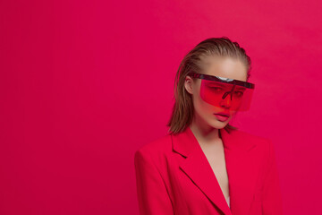 A cool stylish girl with a fashionable hairstyle and stylish glasses with a large glass poses on a bright red background