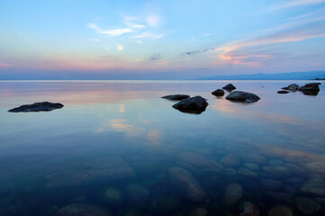 Fototapeta na wymiar Lake Baikal in the summer at sunset. In the foreground is clear water and stones under water.