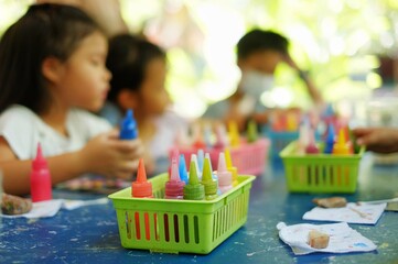 An out of focus picture of a group of students taking an art lesson with colorful paint bottles at the foreground.