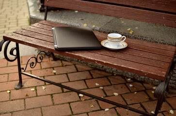 
laptop and cup of tea on a bench in a city park.