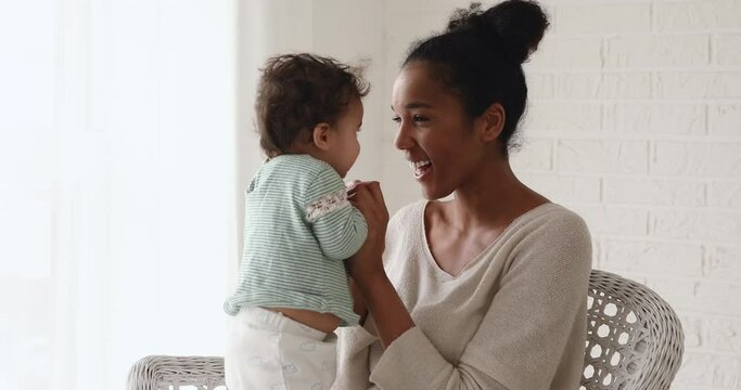 Loving young happy african american mommy holding hands of adorable little toddler kid son, having fun together indoors. Smiling joyful biracial mother playing with cute small child daughter at home.