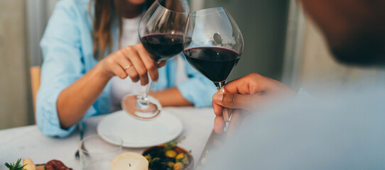 Cropped image of young romantic interracial couple making cheers with glasses of red wine during date in restaurant, Love Relationship Celebration Concept