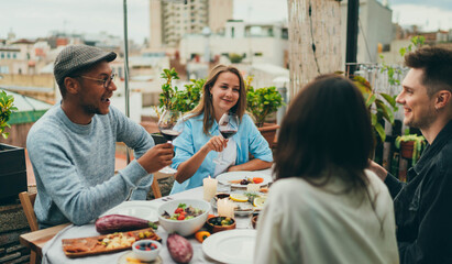 Fototapeta na wymiar Happy Friends at dinner party outside, Interracial group of people having fun together drinking wine laughing and enjoying holidays, Positive people dining together, Friends celebrating rooftop party