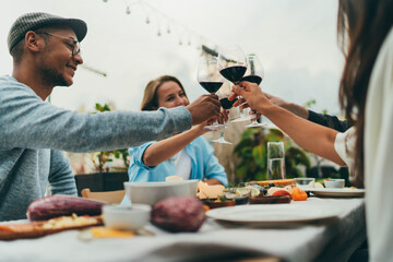 Summer Dinner Party Outdoors, Group of people making cheers with red wine glasses celebrating...
