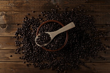 Coffee beans with spoon and clay pot on wooden plank table surface, background and texture, top view