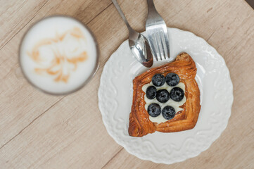 Cold black coffee with ice cubes in tall glass and fresh croissant. Refreshing coffee drink on a table gray background.
