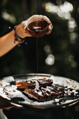 Photo of woman hands holding dark plate with waffle, ice cream, peanuts. Girl holds wooden bowl with maple syrup