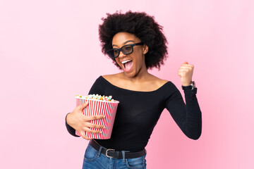 Young African American woman isolated on pink background with 3d glasses and holding a big bucket...