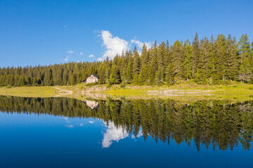 Small alpine chalet immersed in the woods is reflected in the lake.
Holidays in Valtellina, Palù lake. Valmalenco