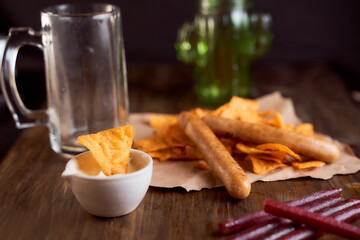 Mexican corn chips nachos lie on a wooden table. One thing in a bowl with sauce