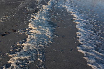 sea foam on sandy beach during sunrise golden hour