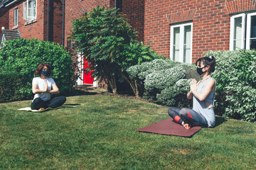 Fototapeta premium Two woman are doing yoga while wearing face masks and keeping the social distance at the garden, stay home and keep the distance concept, new normal