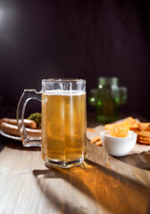 A mug of light beer on a dark background with snacks. Close-up