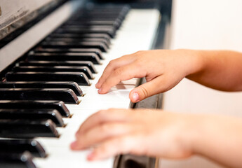 Obraz premium Close up of a little student's hands is playing, learning and practicing the piano. Piano chords In the key of C major. Music abilities for kids. Hobby and activity for the children. Selective focus.
