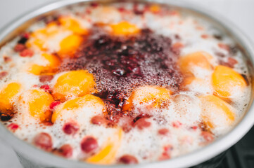 Fresh fruits: apricots, cherries, raspberries, apples are boiled in boiling water in a metal pan on a stove with bubbles and foam close-up. Cooking delicious homemade compote. Photography, concept.