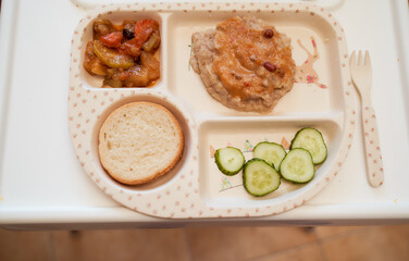 Children's plate in the form of a tray with vegetable stew, steam, bread and cucumbers. Top view