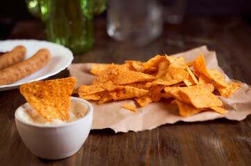 Mexican corn chips nachos lie on a wooden table. One thing in a bowl with sauce