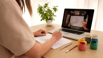 Woman learning to draw on an online course online sitting at home looking over her shoulder. Drawing lesson online on a laptop works on a computer - obrazy, fototapety, plakaty