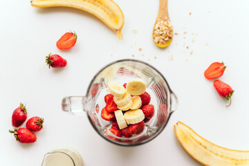 glass blender bowl filled with chopped fruit for a smoothie drink. top view. on the background are ingredients (bananas, strawberries, oat milk) Superfoods and healthy lifestyle or detox diet, vegan