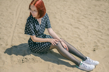 Young woman in black dress sitting on sand and enjoys sea.