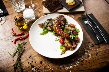 Warm octopus salad with stir fried vegetables and aji sauce on white plate. Delicious healthy mediterranean traditional seafood closeup served on a table for lunch.