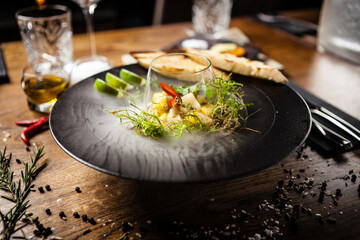 Scallop ceviche with mango, chilli and cilantro served with liquid ice smoke in a plate. Delicious healthy food closeup served for lunch on a table in modern gourmet cuisine restaurant