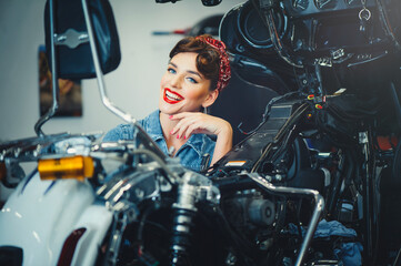 Naklejka na ściany i meble beautiful girl posing repairs a motorcycle in a workshop, pin-up style, service and sale