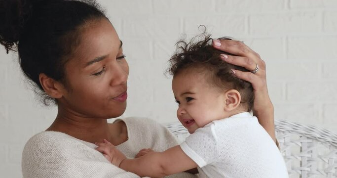 Head shot young african ethnicity mother holding on hands cute funny biracial infant kid daughter, showing love and devotion. Affectionate mixed race mum having fun with sweet adorable child son.