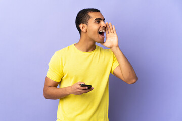 African American man over isolated purple background using mobile phone shouting with mouth wide open