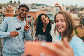 Happy friends taking funny  self portrait on cellphone during rooftop party, Multiracial group of people making funny faces smiling and laughing taking selfie on smartphone to share in social networks