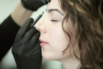 Obraz premium Eyebrow master colors eyebrows, doing permanent makeup. Woman doing makeup while working in black gloves in a beauty salon. Eyebrow concept. Close up portrait. Girl face