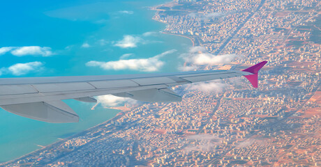 Airplane Wing in Flight view from airplane window a city with the coast in the background