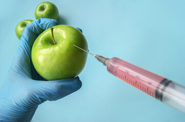 Green apple and syringe with GMO in hands on a blue background.