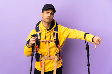 African American man with backpack and trekking poles over isolated background showing thumb down with negative expression