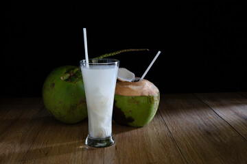 Young coconut and juice of young coconut in glass, all put on brown wooden table which has black background dim light