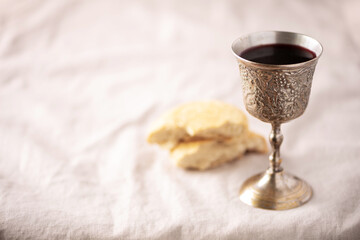 Unleavened bread, chalice of wine, silver kiddush wine cup on canva background. Communion still...