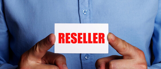 In the hands of a man is a card with the word reseller. Business concept