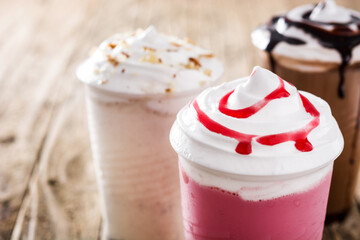 Strawberry, chocolate and white iced milkshakes on wooden table