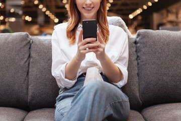 Cropped shot of a woman smiling, using smart phone while resting on a sofa
