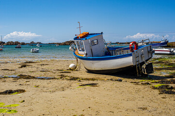 Naklejka na ściany i meble Fishing boat on a beach in Brittany. Sandy beach strewn with seaweed.