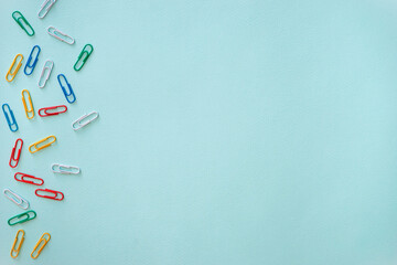 Multi-colored paper clips arranged randomly in the left part of the photo. Objects of white, yellow, green, red and blue colour. Horizontal photo. Flat lay composition on a light blue background