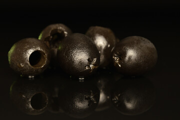 Pickled spicy black olives, close-up, on a black background.