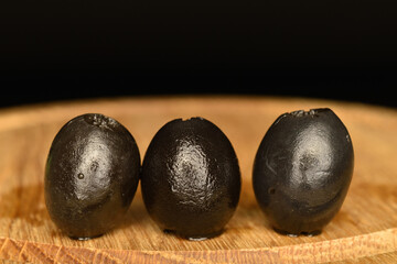 Pickled spicy black olives, close-up, on a black background.