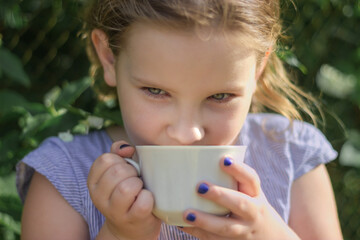 Happy little girl tastes aromatic flower tea from white cup