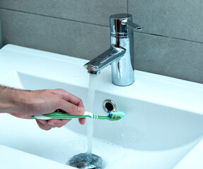 Man taking a toothbrush in a sink to clean up