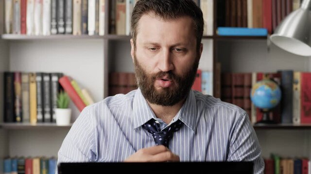 Heat, excitement, deadline, nervous tension concept. Sweating man in wet shirt and plain look is working at computer, he is hotly muffled and uncomfortable, drinks water and is worried. Close-up