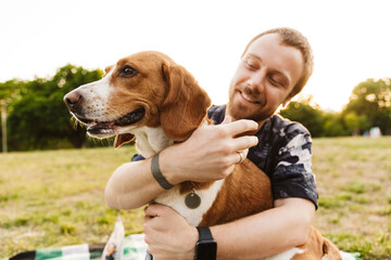 Image of young man smiling and sitting with his beagle dog in park